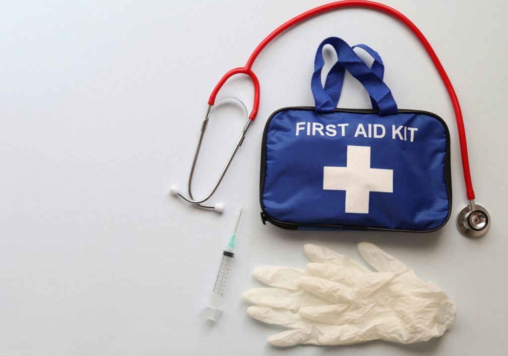 Flat lay of first aid kit, stethoscope, syringe, and gloves on white background.